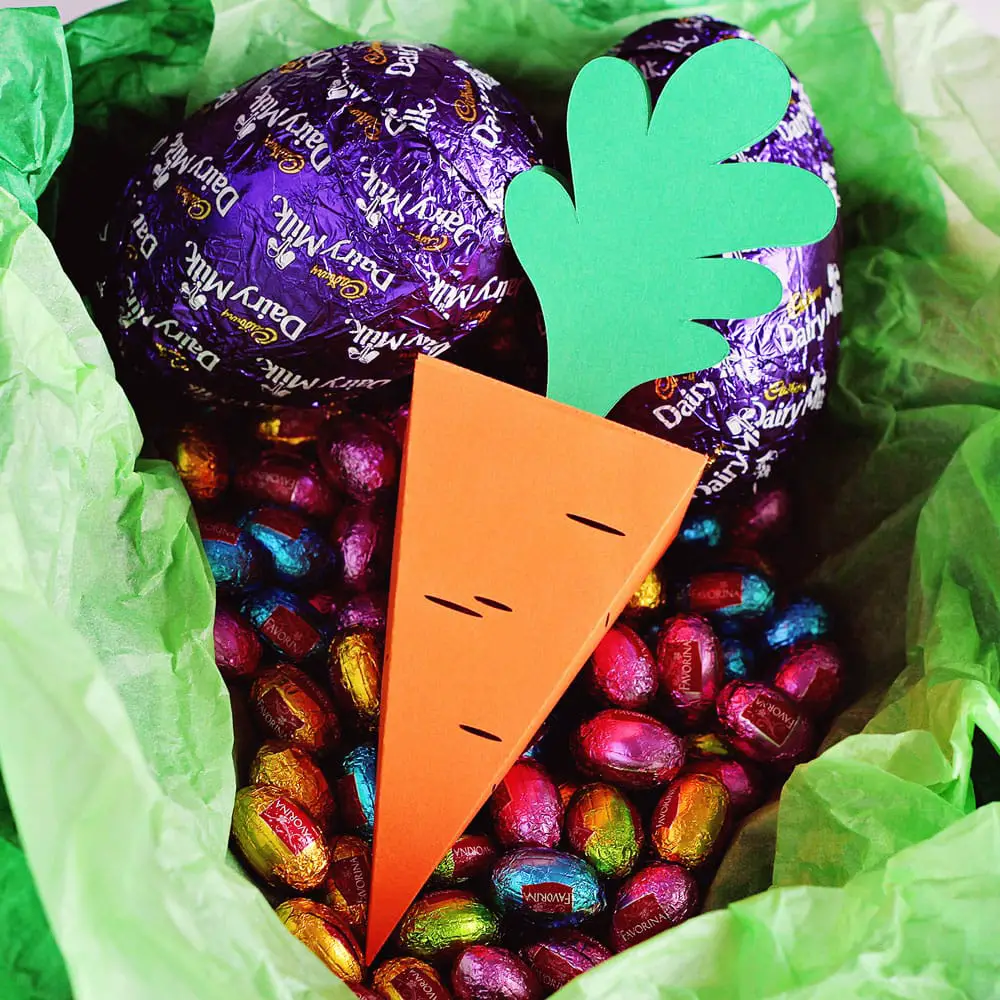 DIY Easter carrot treat box in a basket surrounded by chocolate eggs