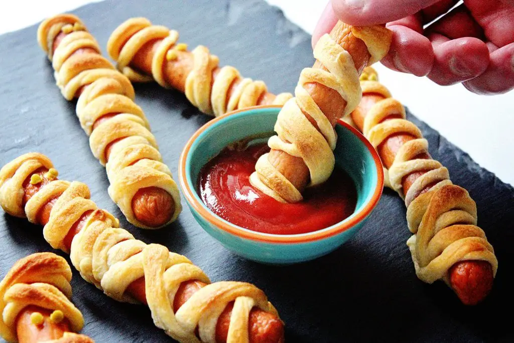 Halloween mummy hot dogs being dipped in ketchup