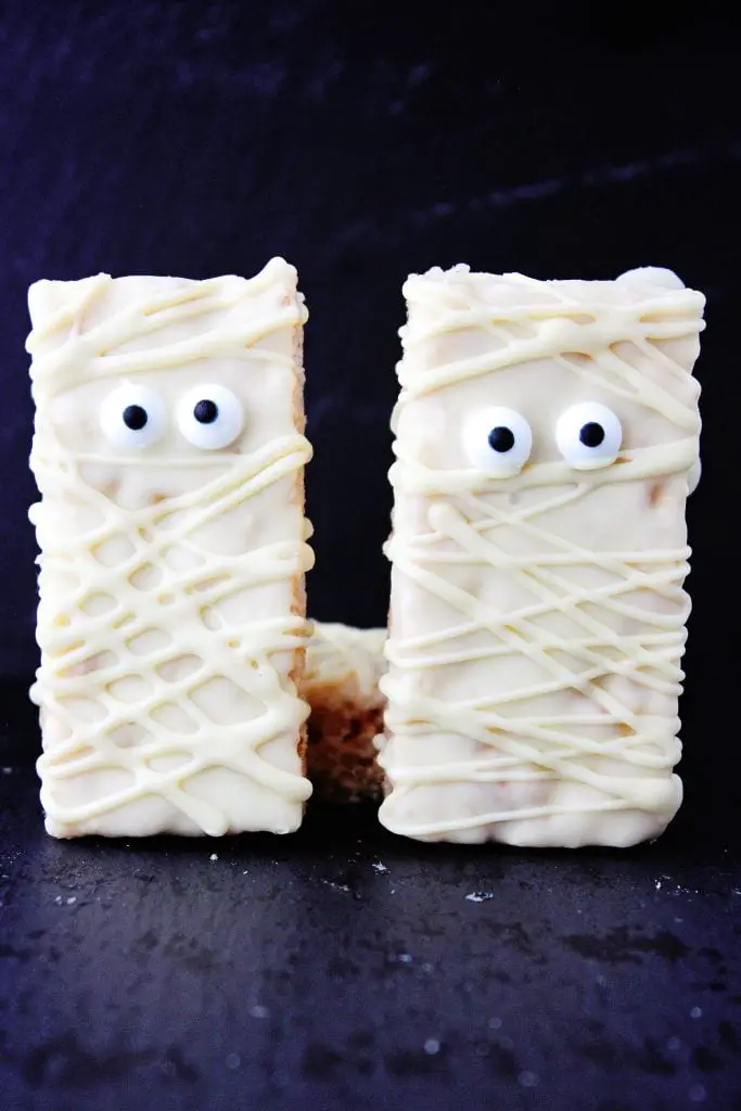two mummy rice krispie treat snacks propped upright against a dark background