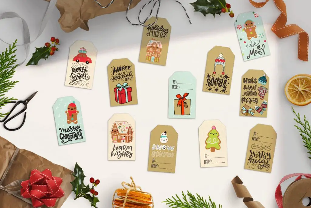 top view of 12 cute free printable Christmas gift tags lying on a white table surrounded by gift wrap, holly and, ribbon, dried oranges and leaves