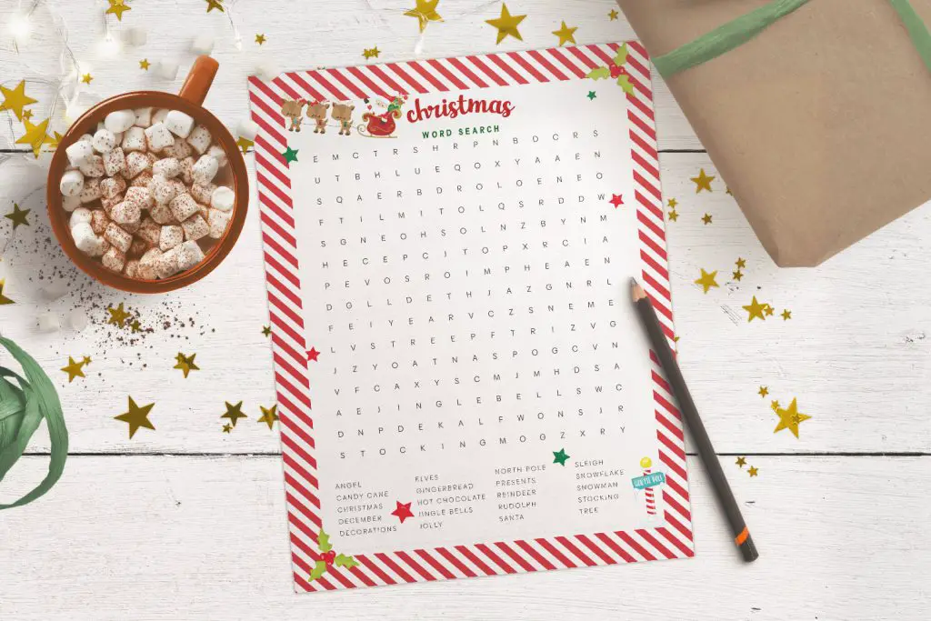 Christmas word search printable on a white table, with a pencil, Christmas gift, mug of hot chocolate and gold stars scattered around