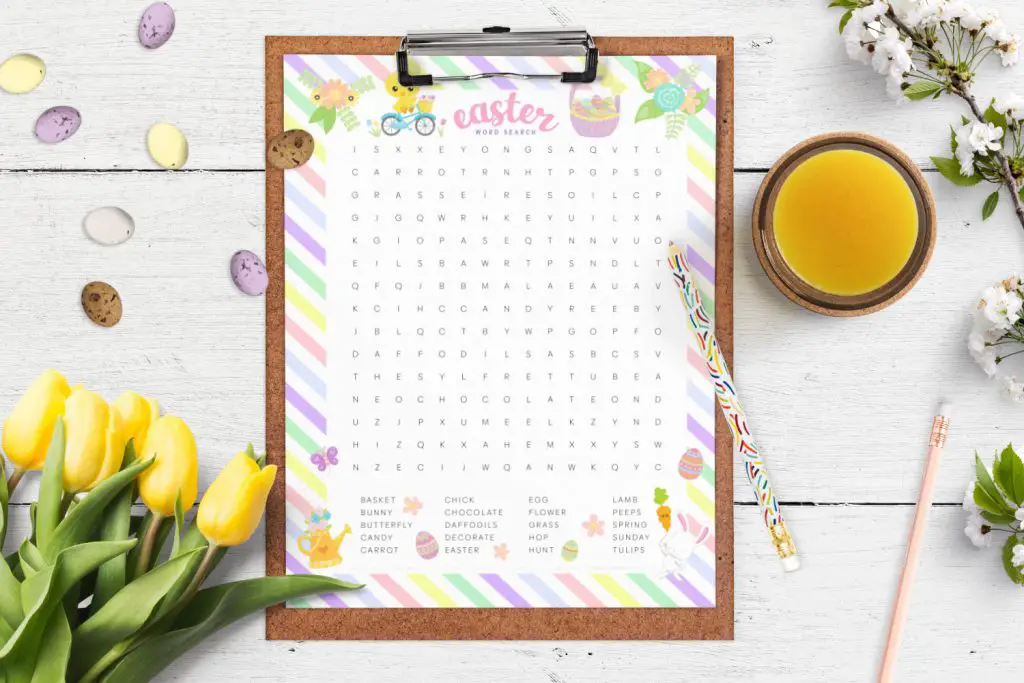 a clipboard with the Easter word search printable lying on a table with spring flowers, candy eggs and pencils