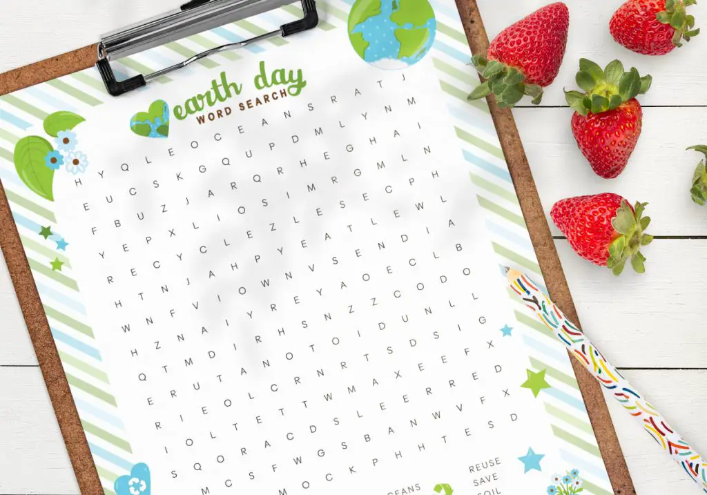 Close up of the free printable earth day word search on a clipboard lying on a table, with a colorful pencil and some strawberries